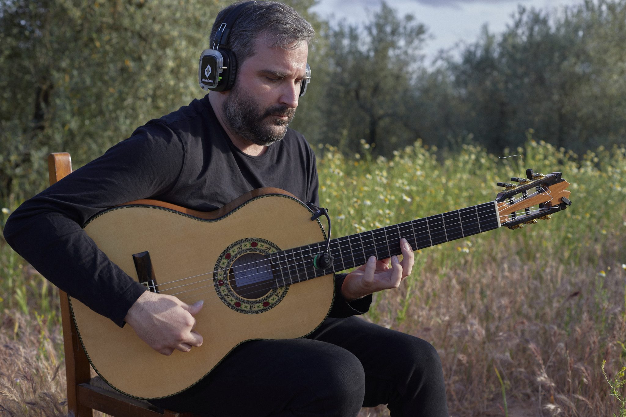 Eduardo Trassierra tocando la guitarra con auriculares en el olivar de La Aceitera