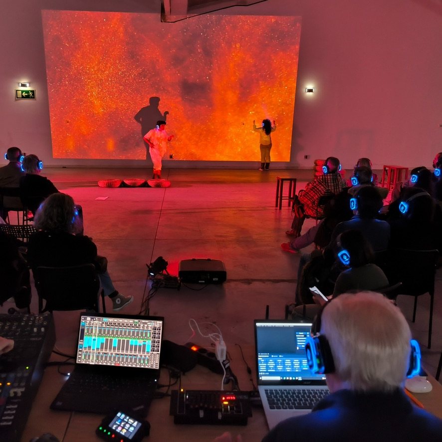 Intérpretes de Al Otro Lado ante la proyección de gran formato, con el público escuchando por auriculares